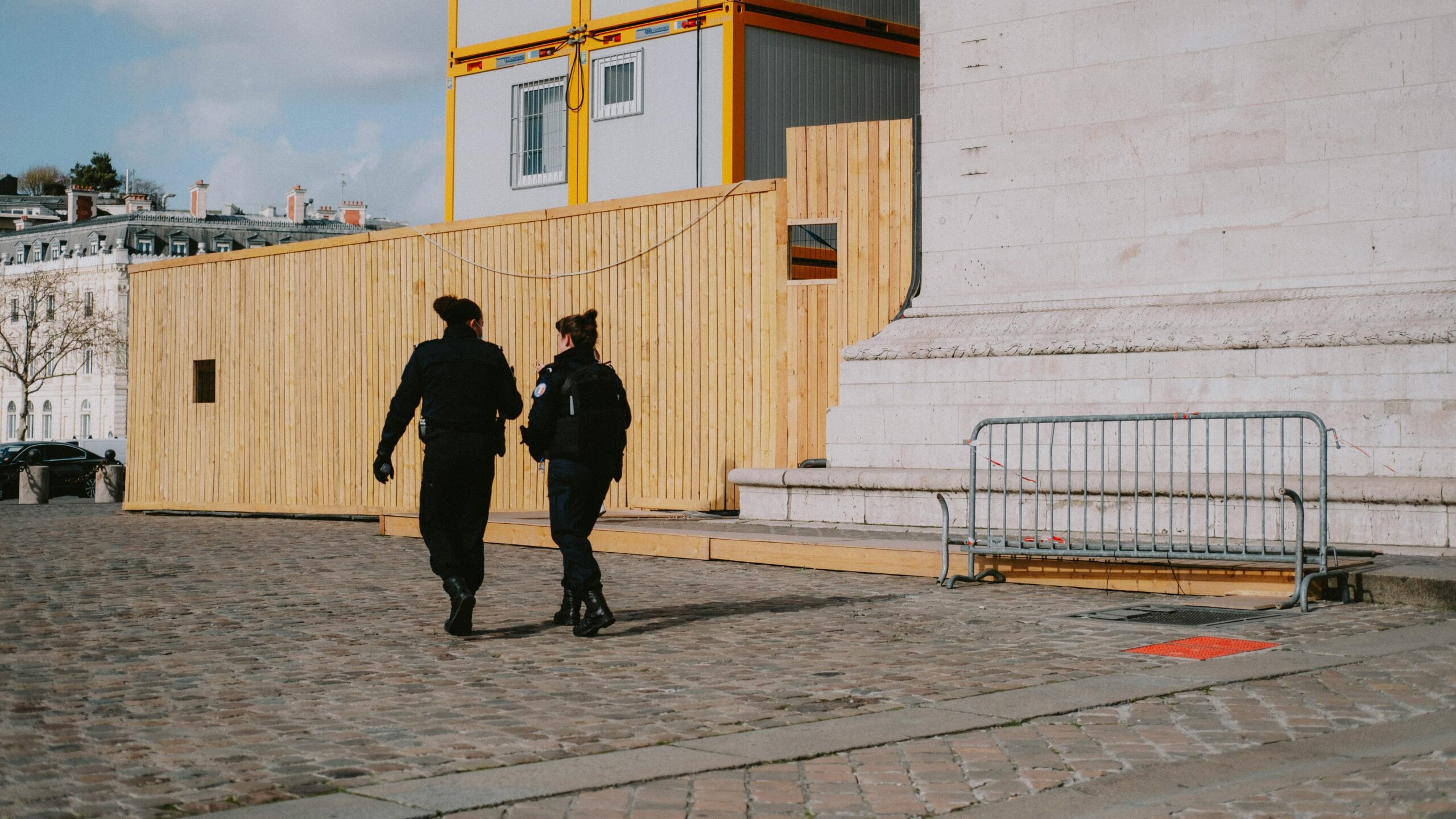 accueil Two police officers walking near a construction site on a cobbled street.